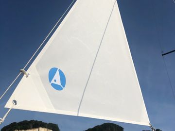 A sailboat with an anchor riding sail. Sail hoisted. Sail against blue sky.