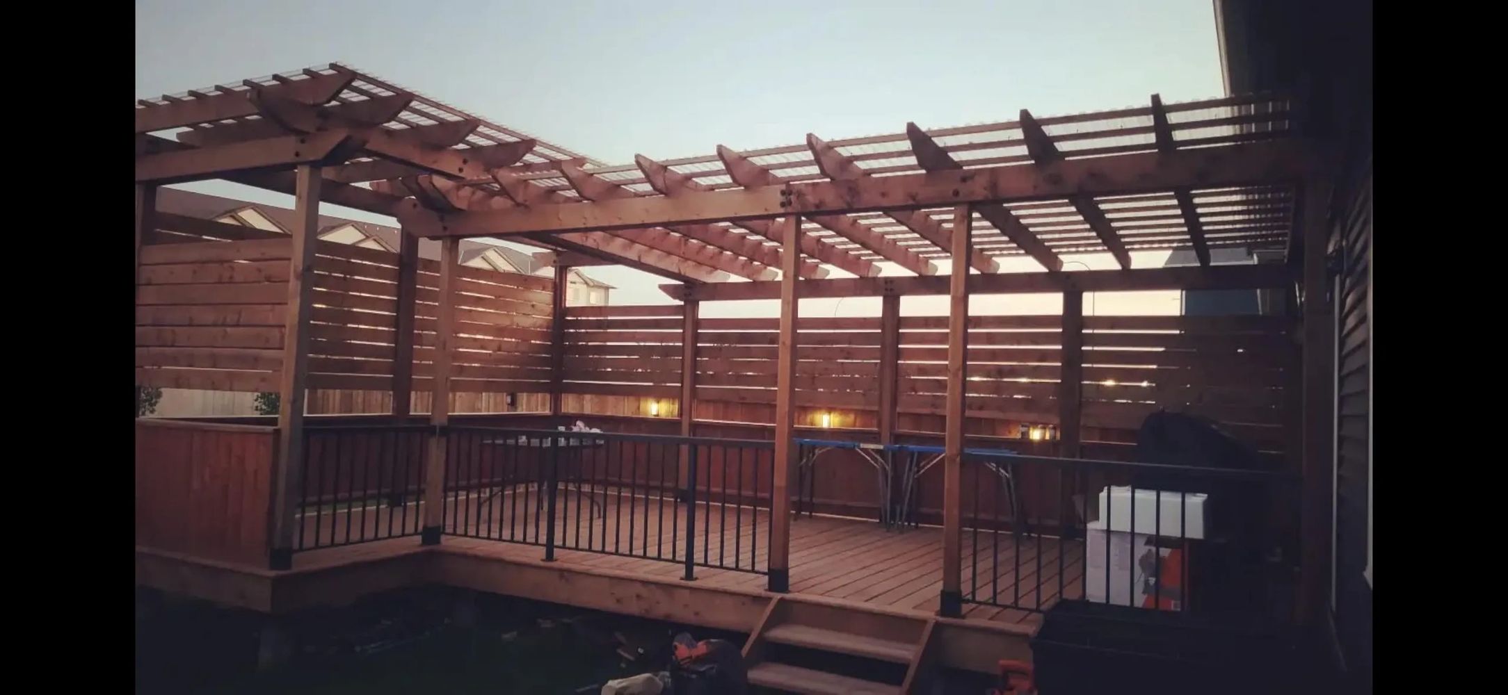 Wooden deck with pergola and privacy fence in a backyard.
