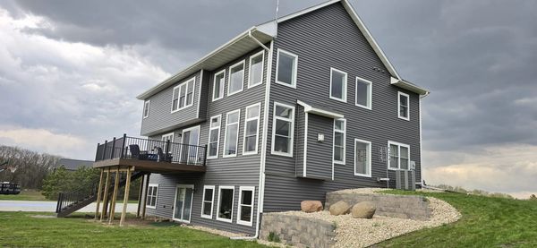 Modern two-story gray house with elevated deck and stormy sky.