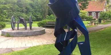 Blue spiral sculpture in a green garden with a historical cannon in the background.