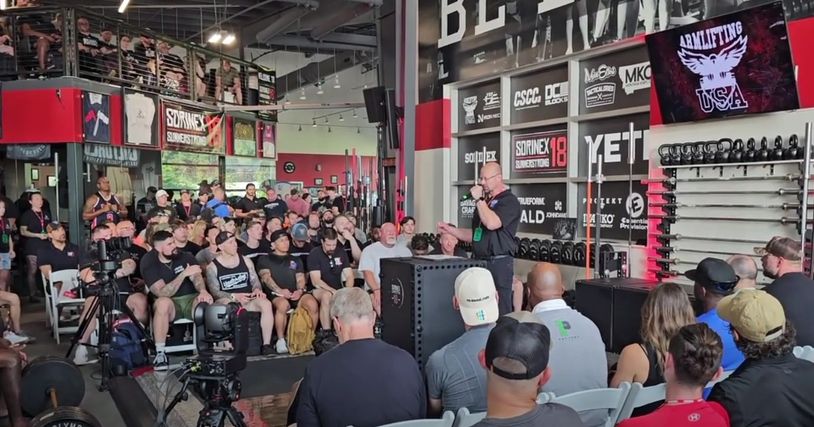 Crowd listening to a speaker at a fitness event in a gym.