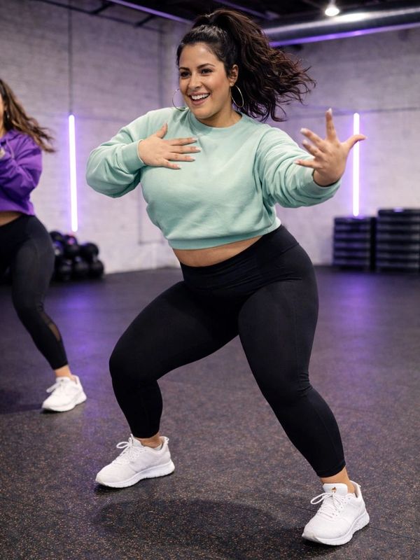 A woman enthusiastically dancing in a gym setting, wearing workout clothes.