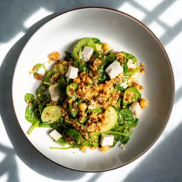 Fresh quinoa salad with spinach, chickpeas, zucchini, and tofu cubes in a white bowl.
