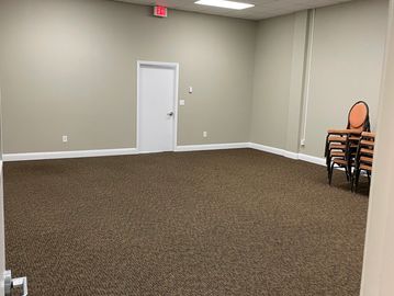 Empty room with brown carpet and stack of chairs in the corner.