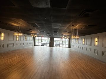 Empty room with wooden floor, dark ceiling, and modern chandeliers.