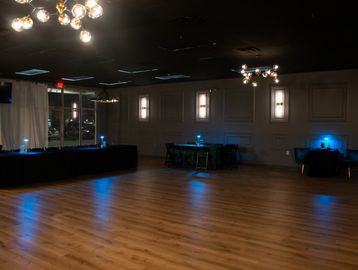 Dimly lit event space with wooden floors and blue accent lights on tables.