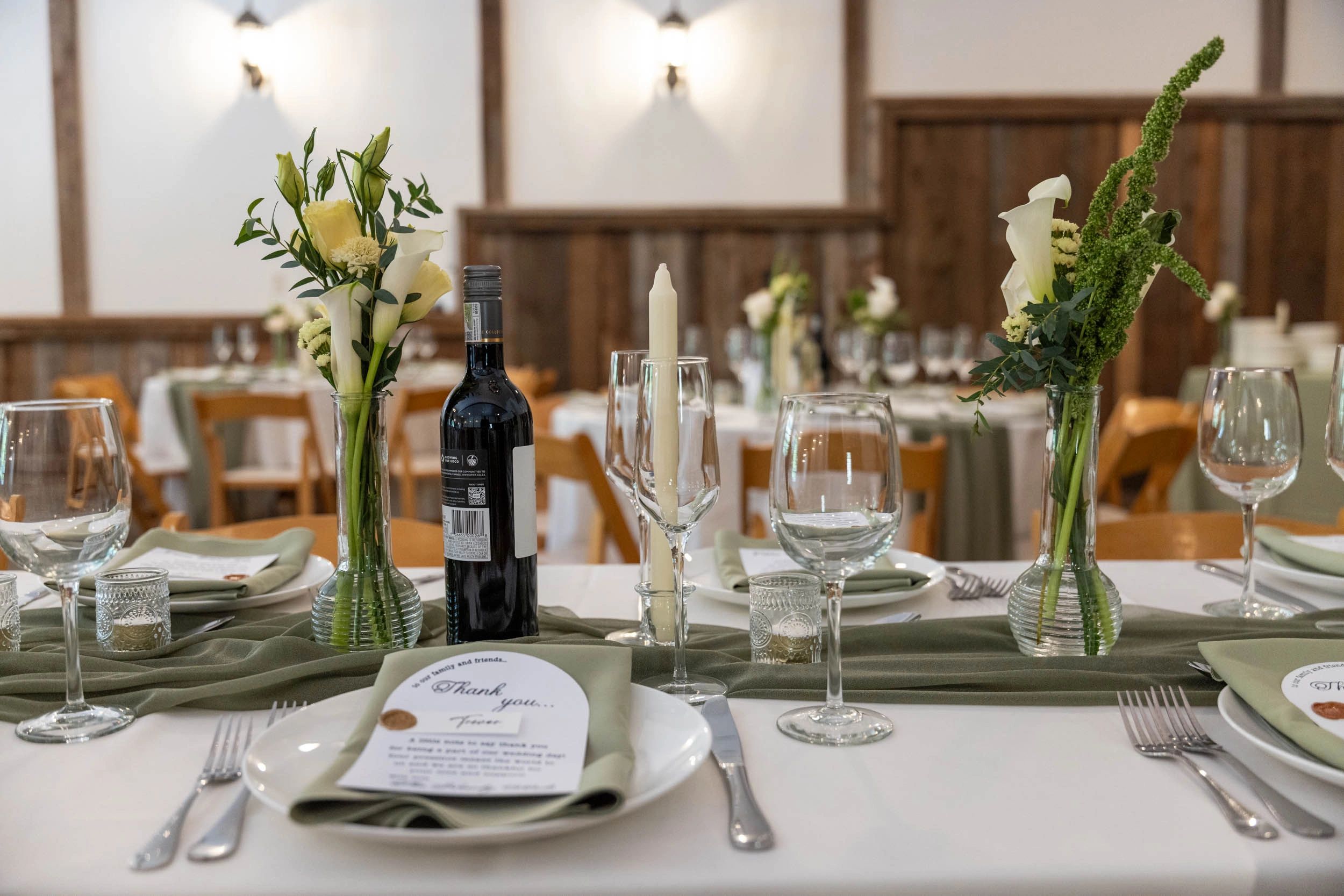 Elegant wedding table setup with flowers, wine, candles, and thank you cards.