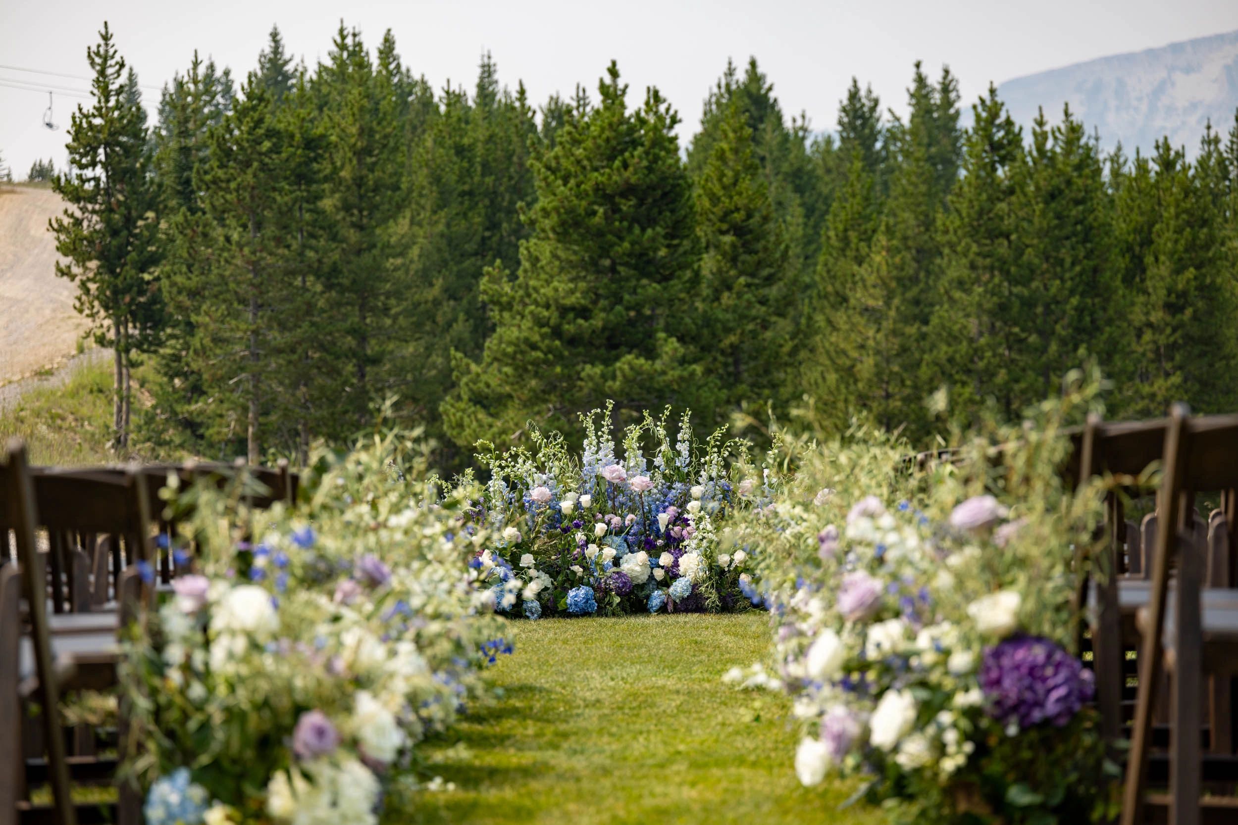 Outdoor wedding ceremony aisle with floral decorations and pine trees.