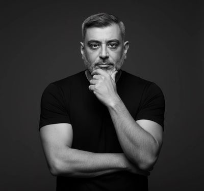 Black and white portrait of a thoughtful man with a beard and short hair, wearing a black t-shirt.