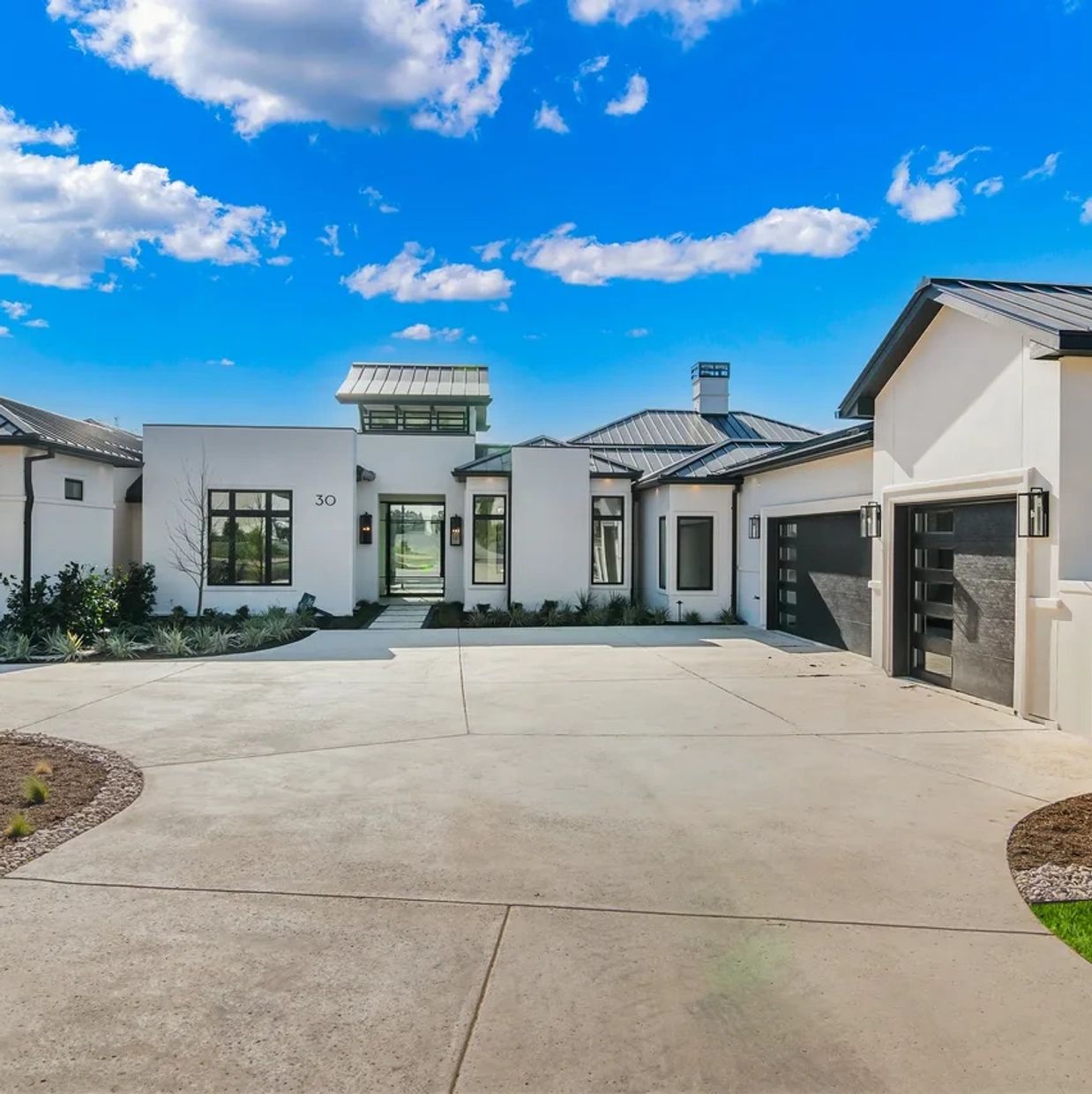 Modern white house with black accents and a spacious driveway under a blue sky.