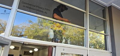 A worker installs privacy film on a large glass window above a door.