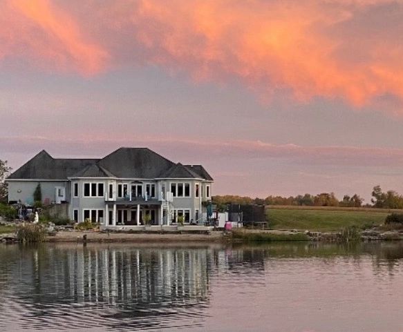 A large house beside a calm lake at sunset with orange clouds.
