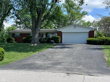 Single-story brick house with a large tree and a wide driveway.