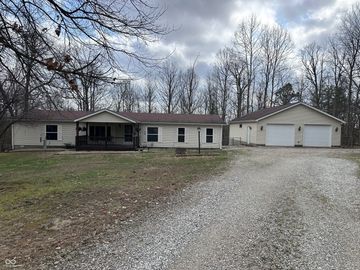 Single-story house with detached garage on a gravel driveway in a wooded area.
