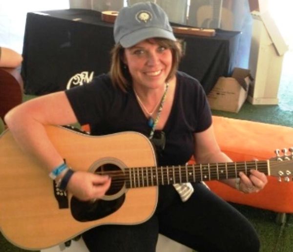 Woman smiling while playing an acoustic guitar indoors.