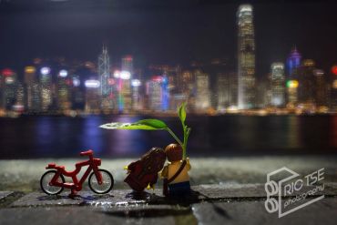 Toy figures with a plant beside a red bicycle at night cityscape.