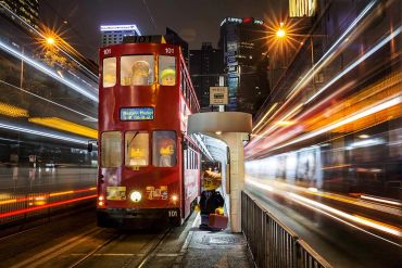 Red tram in a city at night with light trails.