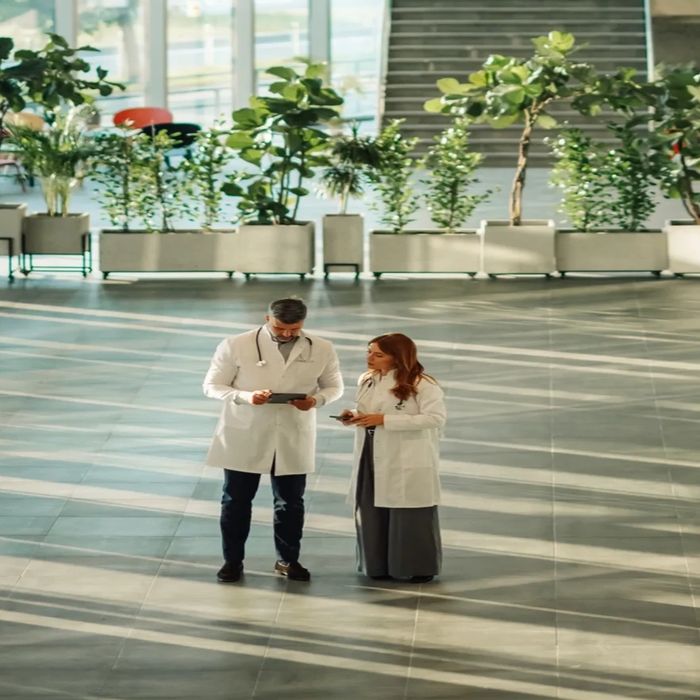 Two doctors discussing notes in a spacious, modern atrium filled with plants.
