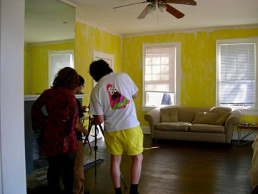 Two people in a yellow-walled room with a sofa.