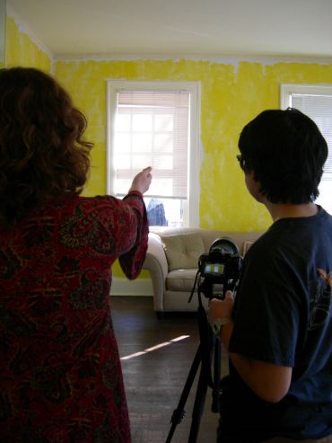 Two people setting up a camera inside a room with yellow walls.