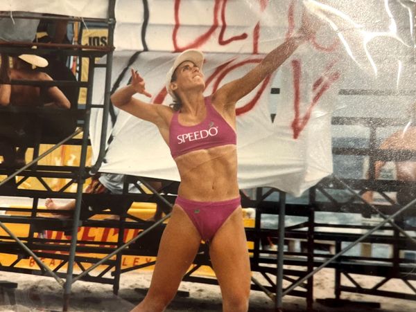Female beach volleyball player in action, wearing Speedo sportswear and a cap.