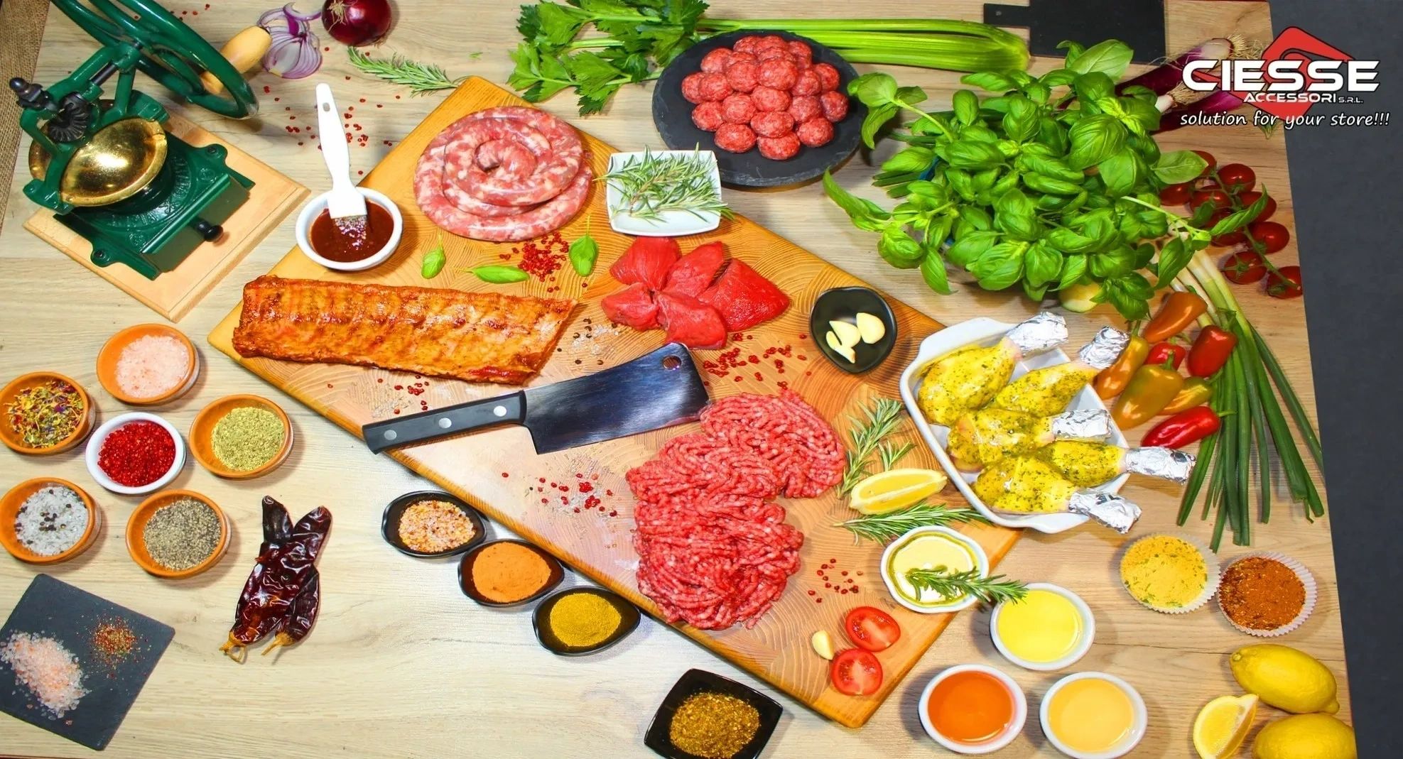 Various meats, spices, and herbs arranged on a wooden board with a cleaver and vintage grinder.
