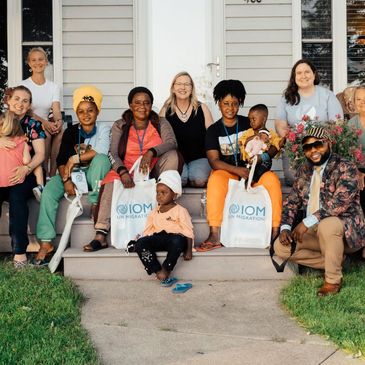 A diverse group of people smiling outside a house holding IOM bags.