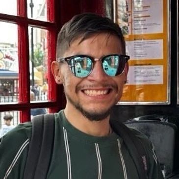 Smiling man wearing reflective sunglasses and a striped shirt indoors.