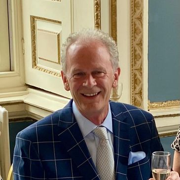 Elderly man in a checkered suit smiling at a formal event.