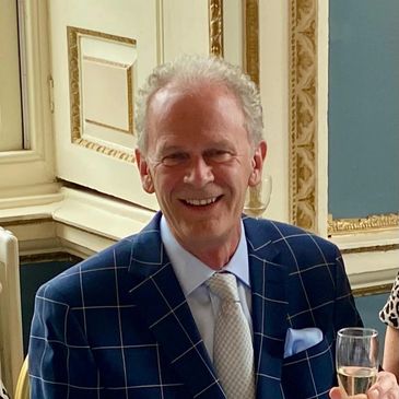 Smiling elderly man in a checked blazer holding a glass at a formal event.