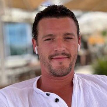 Man in white shirt wearing earphones, smiling outdoors.