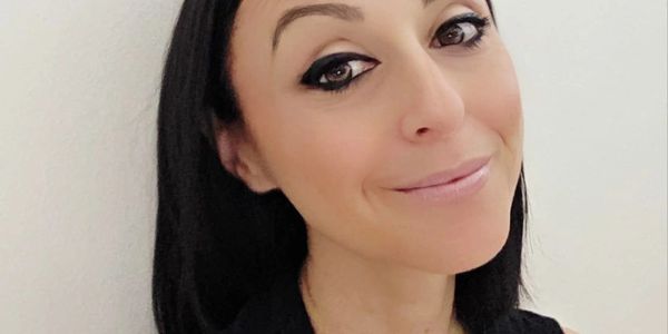 Woman with dark hair and winged eyeliner smiles softly at the camera.