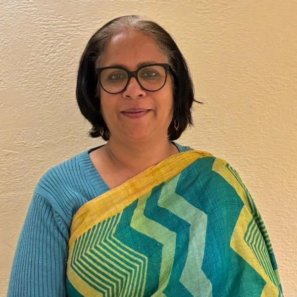 Woman wearing glasses and a blue-green patterned sari, smiling gently.