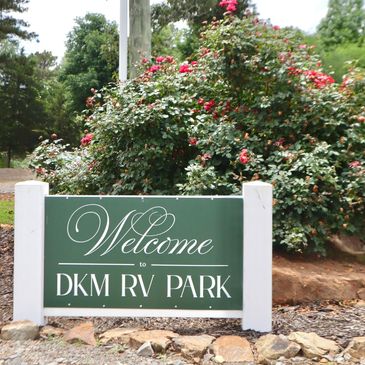 Welcome sign for DKM RV Park with lush greenery behind.