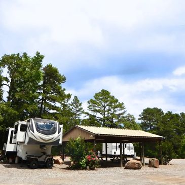 RV parked next to a covered picnic area in a wooded campground.
