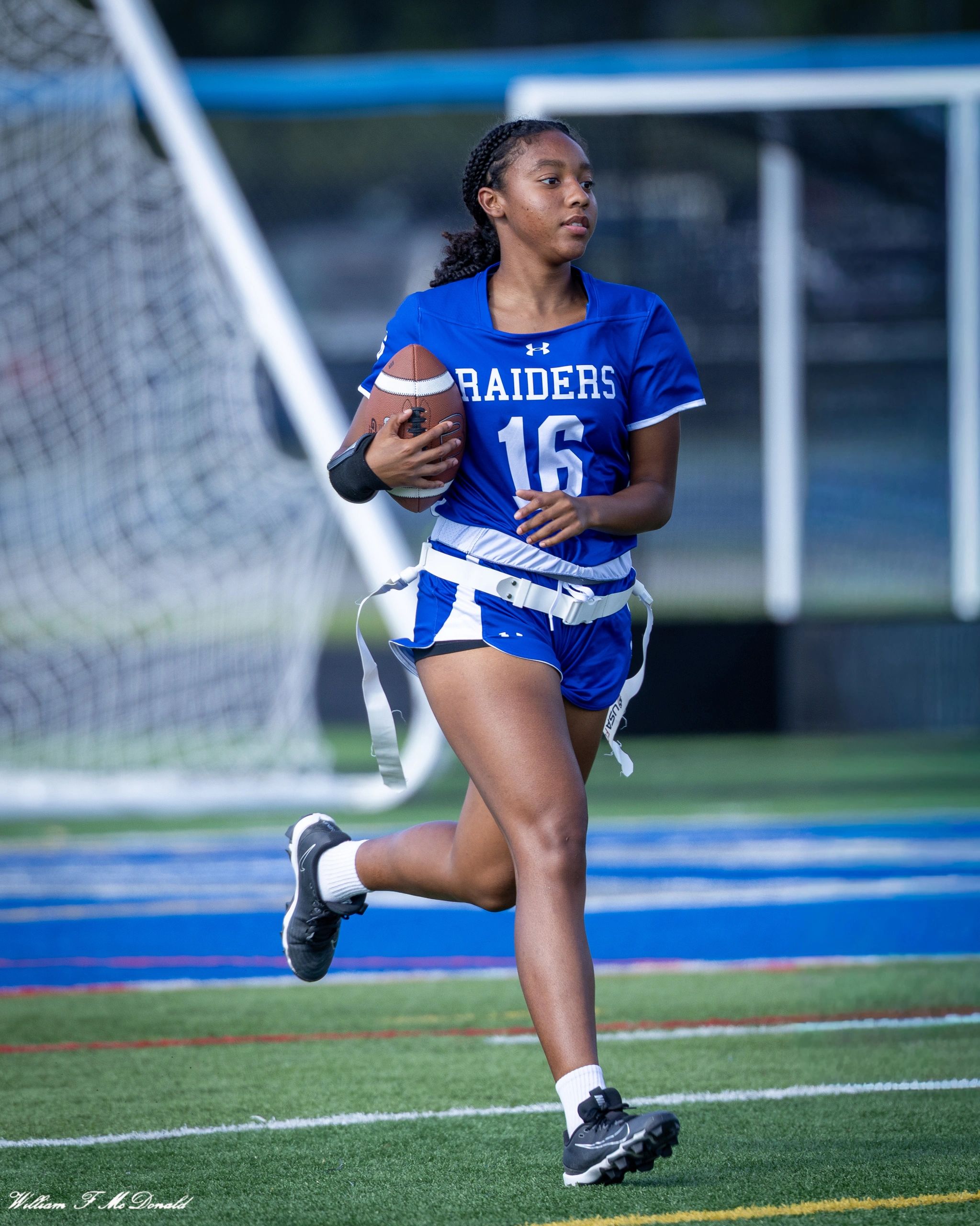 Girl in blue Raiders jersey running with football on field.
