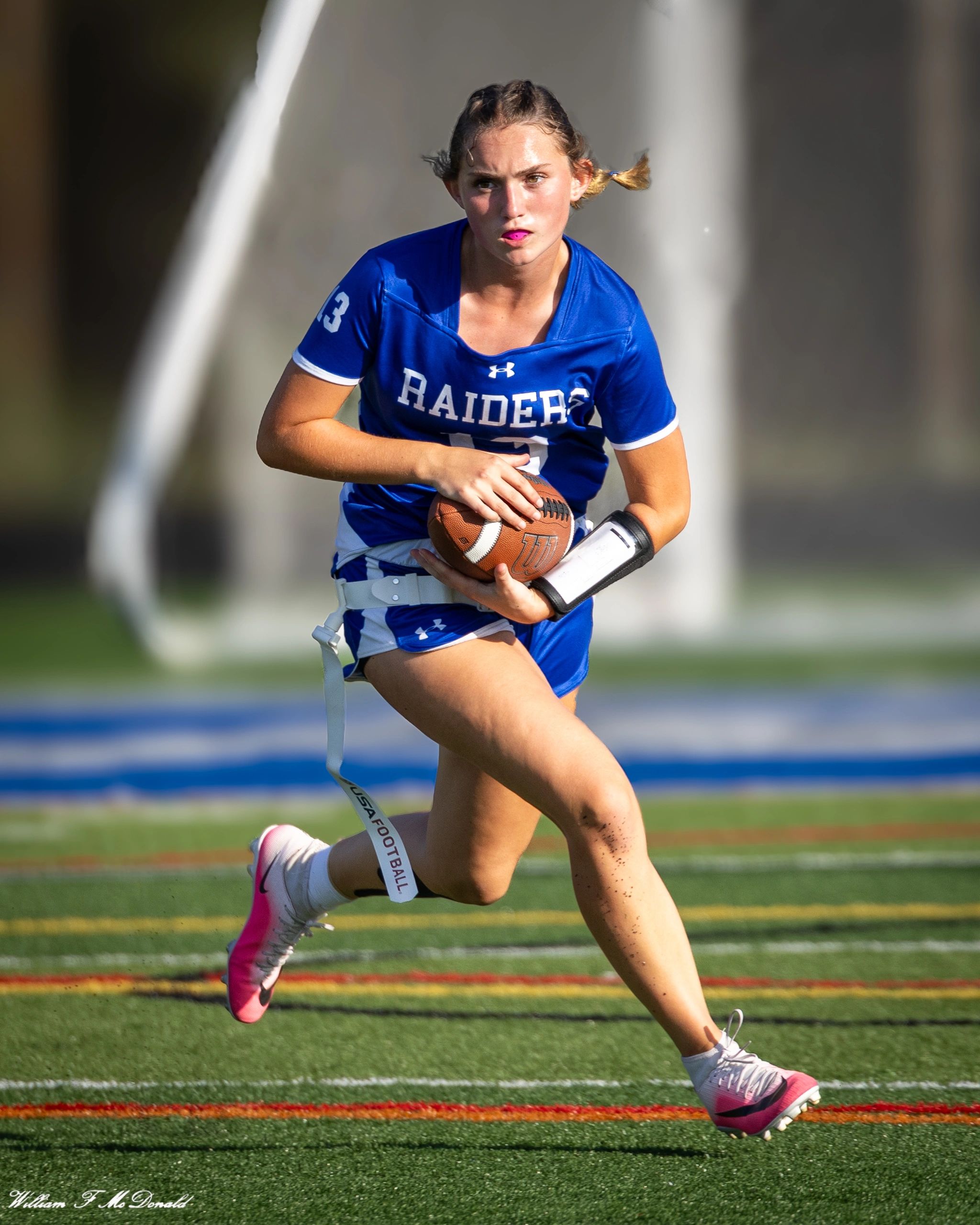 Female athlete running with football on field.