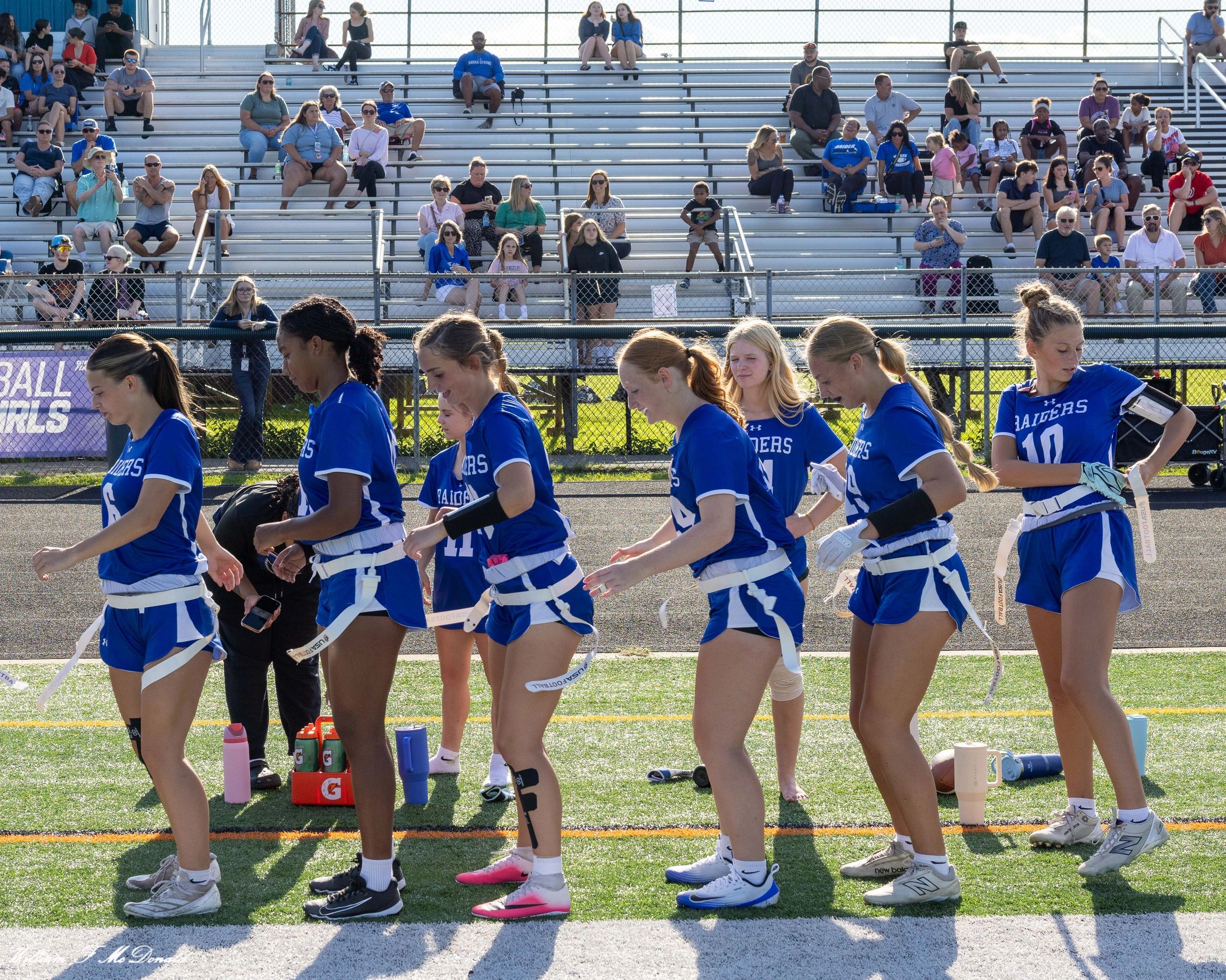 Flag football team warms up before game with audience in stands.