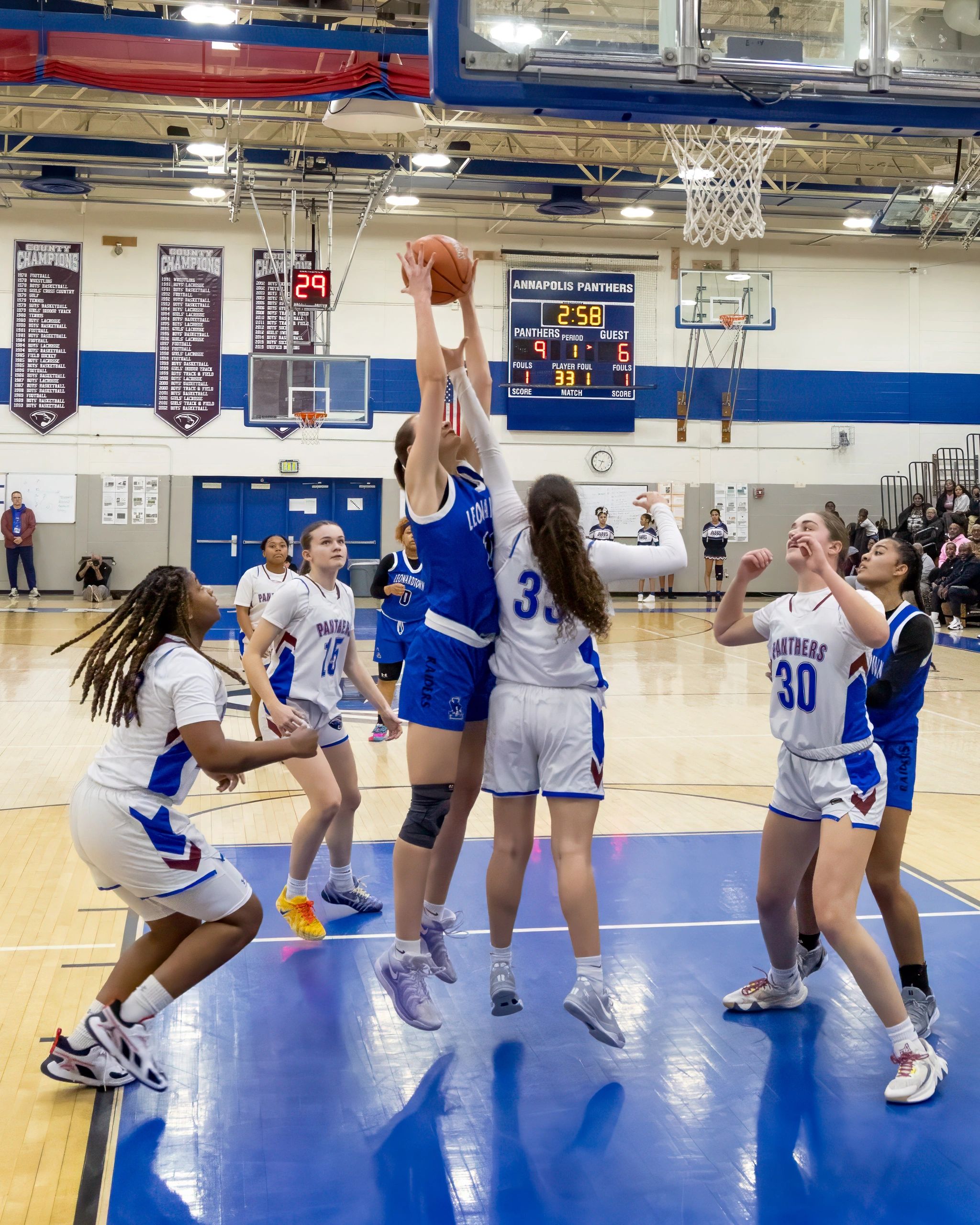 Girls' basketball game action near the hoop in a gymnasium.