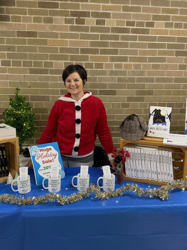 Woman in red sweater at a holiday sale table with mugs and books.