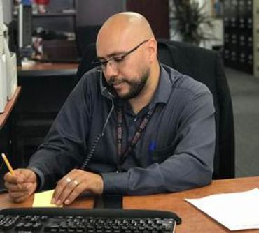 Notary Public Cesar J. Navarro, at office desk, on the phone with a client writting down information