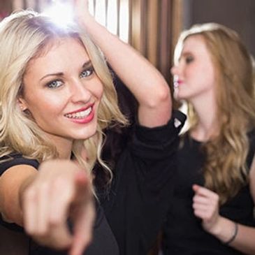 Happy young woman pointing and smiling at the camera during a party.