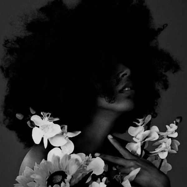Black and white portrait of a woman with voluminous hair surrounded by flowers.