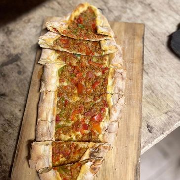 Sliced Turkish pide with vegetables on a wooden board.