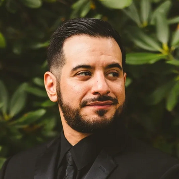 Photo of justPEREZplay in Black Suit & Tie in front of Green Bush