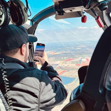 Photo of justPEREZplay  recording video on an phone in a helicopter hovering over a Tulip field.