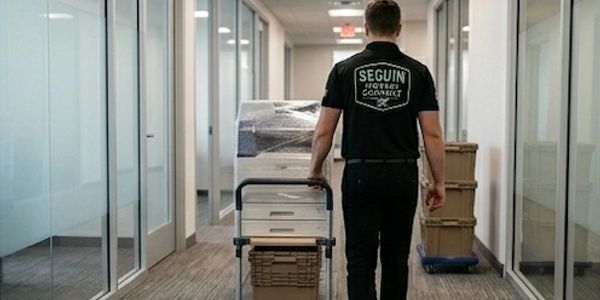 Worker pushing a cart loaded with boxes down an office hallway.