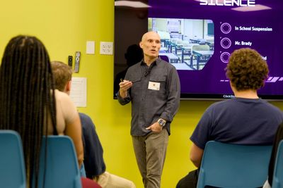 Man giving a presentation to a seated audience in a bright room.