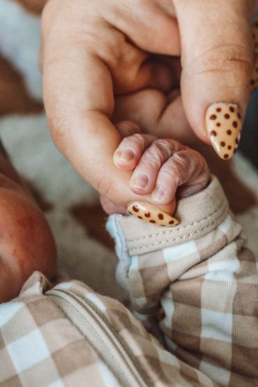 A baby holding an adult's finger with matching polka dot nails.