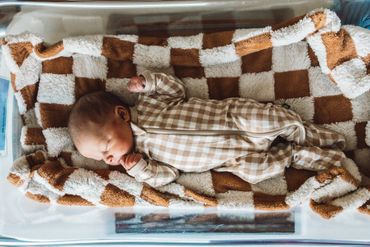 Newborn baby sleeping peacefully on a soft checkered blanket.